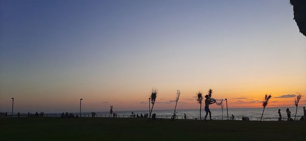 Silhouette people on beach against clear sky during sunset