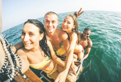 Fish-eye lens portrait of happy friends on boat ladder in sea