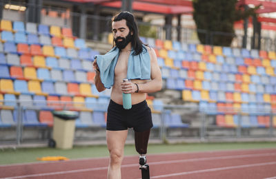 Man with prosthetic leg holding bottle walking on running track