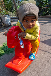 Portrait of cute boy wearing knit hat sitting on toy outdoors