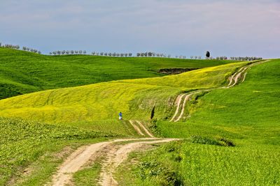 Dirt road passing through landscape against cloudy sky