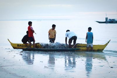 Rear view of men on boat in sea against sky