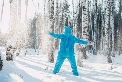 Rear view of man wearing costume standing against trees on snowy field in winter