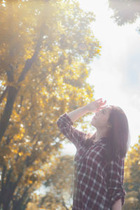 Midsection of woman holding smart phone while standing on tree