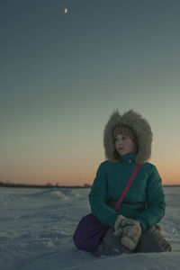 Portrait of woman sitting on snow against sky during sunset