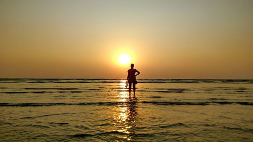 Rear view of silhouette woman standing in sea against sky during sunset