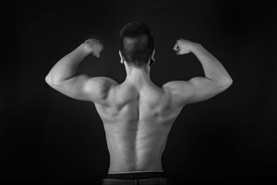 Rear view of shirtless man standing against black background