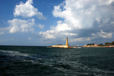 View of lighthouse in sea against cloudy sky