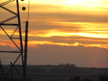 Low angle view of electricity pylon against sky during sunset