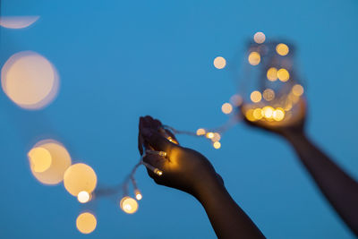 Midsection of person holding illuminated lighting equipment against sky