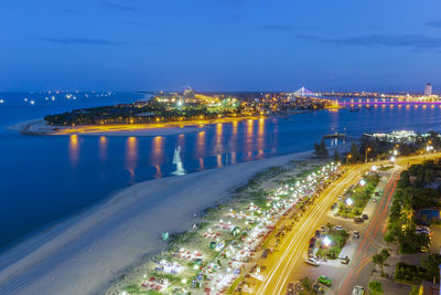 High angle view of illuminated city by sea at night