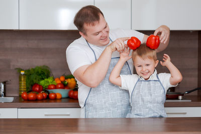 Smiling father and son having fun holding red bell peppers in the form of ears