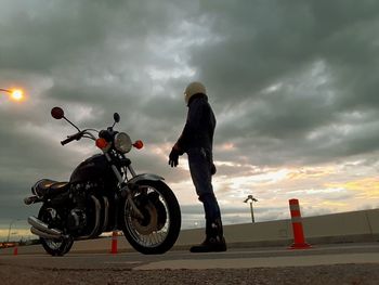 Man riding motorcycle on road against cloudy sky