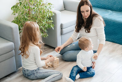 Mother with daughter and baby son playing a game of django on the floor