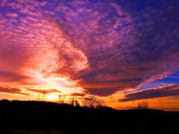 Silhouette trees against dramatic sky during sunset