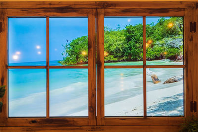 Trees by swimming pool against sky seen through window