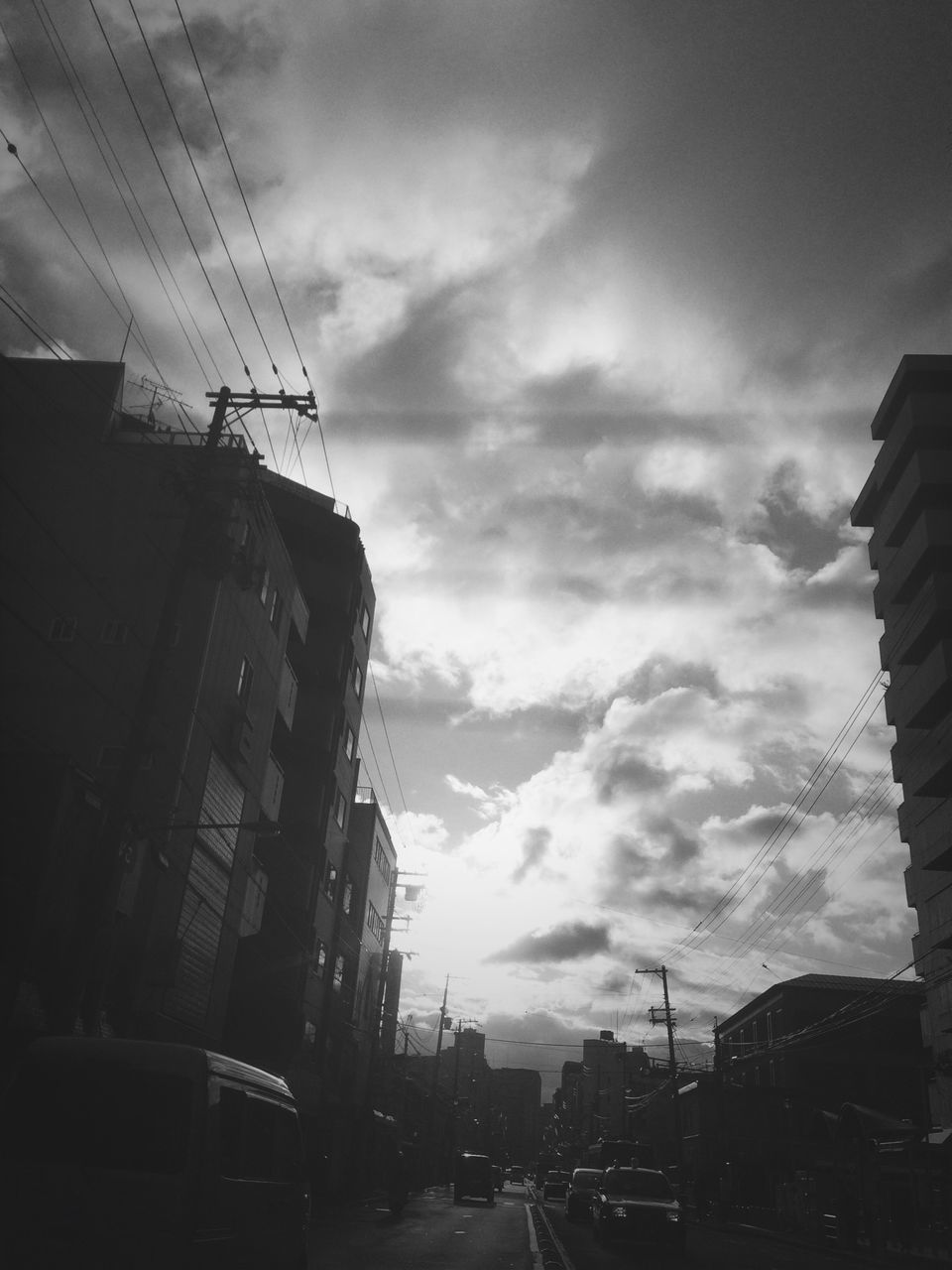 transportation, building exterior, architecture, built structure, sky, land vehicle, mode of transport, car, street, city, cloud - sky, low angle view, road, cloudy, cloud, city life, building, city street, incidental people, street light