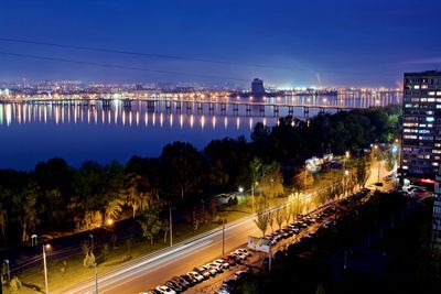 Light trails on road by illuminated city against sky at night