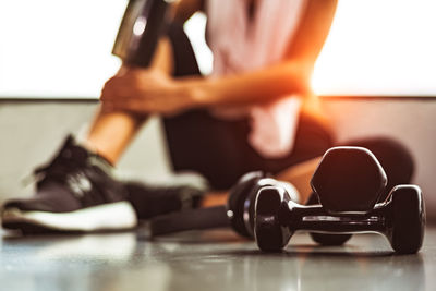 Close-up of dumbbell with woman sitting on floor in gym