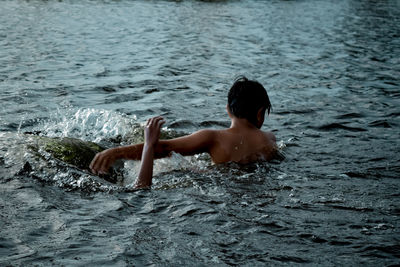 Rear view of shirtless boy swimming in sea