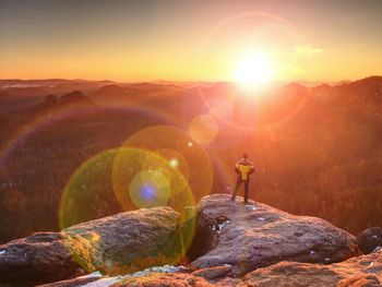 Man on rock against sky during sunset