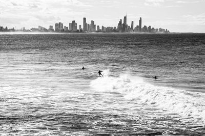 Surfers on sea by city against sky