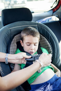 Cropped image of mother fastening seat belt of son's car seat