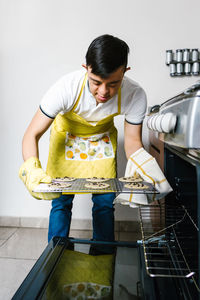 Ethnic teenage boy with down syndrome putting raw chocolate chip cookies in oven while baking pastry in kitchen