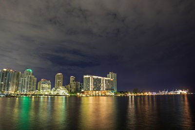 Illuminated buildings by sea against sky at night