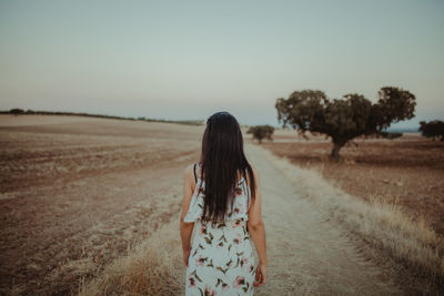 Rear view of woman standing on field against sky during sunset