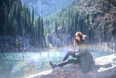 Woman sitting on log by lake at forest