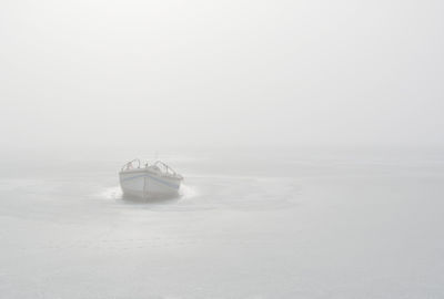 Wooden fishing boat trapped in frozen lake in misty morning