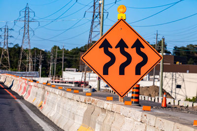 Road sign by railroad tracks against sky