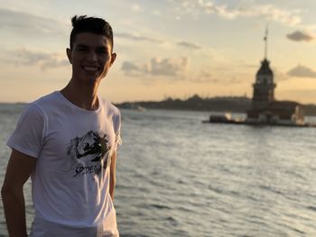 Smiling young man standing against sky during sunset