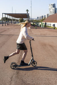 Smiling young woman riding kick scooter