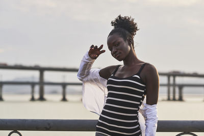 Young woman standing by railing against sky