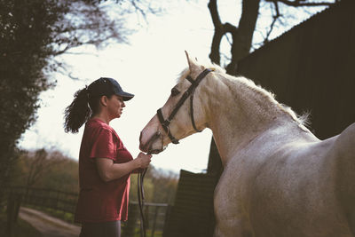 Side view of mature woman standing with horse at barn