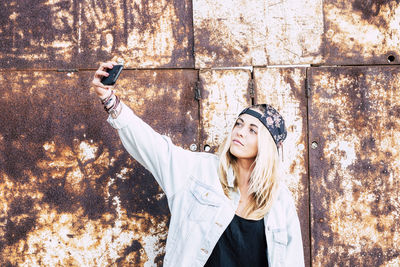 Young woman using mobile phone against wall