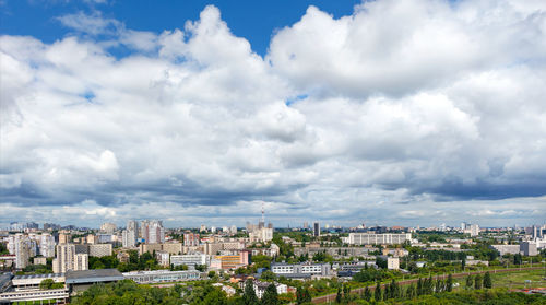 Panorama of kyiv, with high cloudy skies over residential areas, green parks and a tv tower.