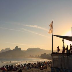 People at beach against sky during sunset