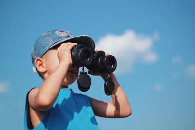Low angle view of boy photographing against blue sky