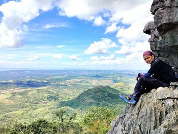 Man sitting on rock against sky