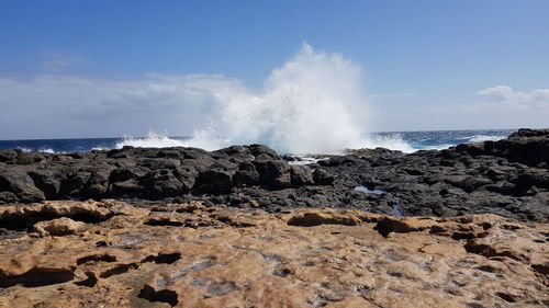 Sea waves splashing on rocks against sky