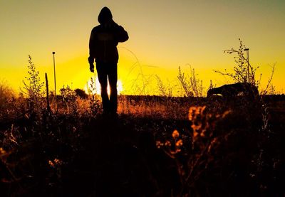 Silhouette man standing on field against sky at sunset