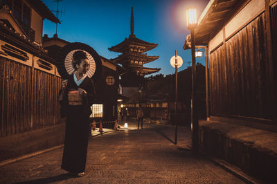 Illuminated street light on footpath amidst buildings in city at night