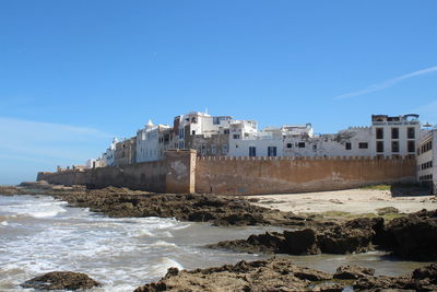 Buildings by sea against clear blue sky