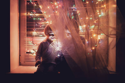 Siblings sitting by illuminated lights and window at night