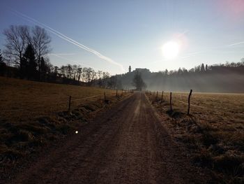 Dirt road amidst field against sky