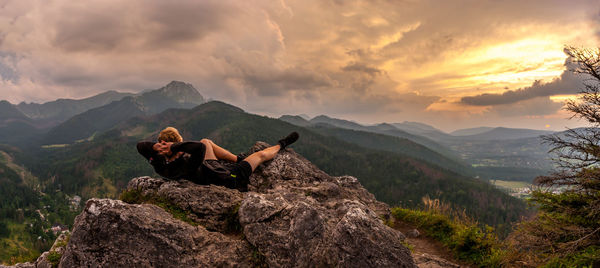 Man relaxing on rock against sky