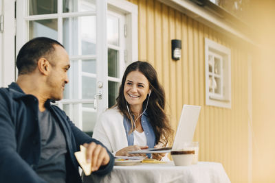 Smiling woman showing laptop to man while sitting at table in patio